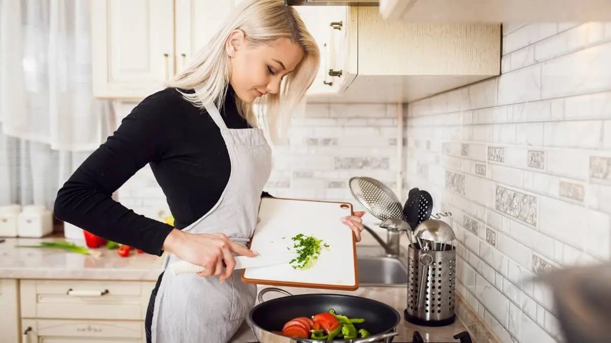 Žena v zástěře přidává nakrájenou cibulku do pánve se zeleninou Žena v zástěře přidává nakrájenou cibulku do pánve se zeleninou